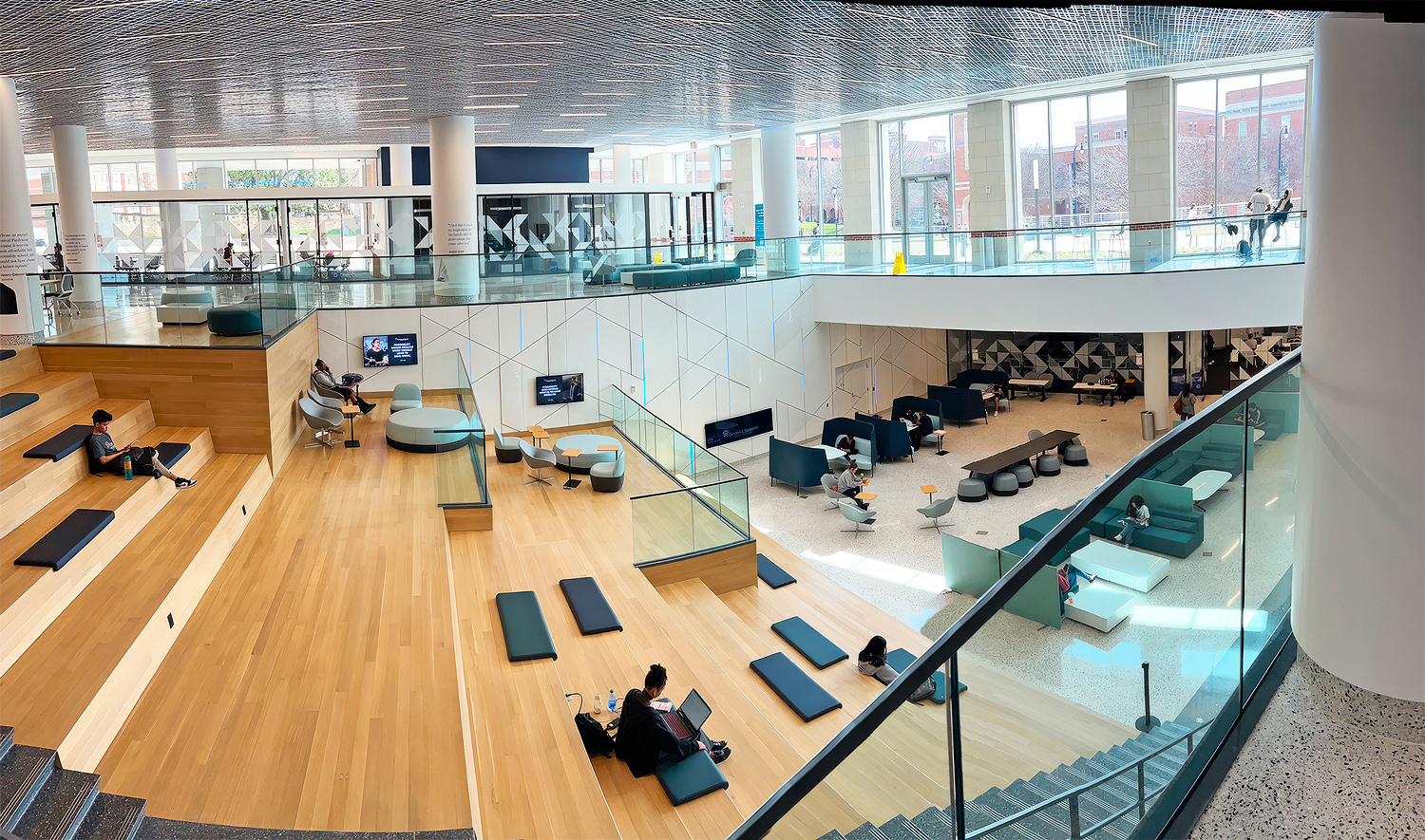 Digital signage displays are mounted at staggered heights along the wall adjoining the collaborative stairs in the student commons.