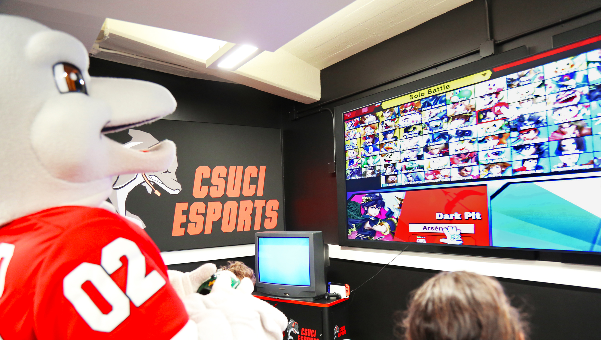 Visitors and CSUCI’s dolphin mascot observe gaming action on one of three spectator displays in the esports lounge during the open house that followed the ribbon cutting event.