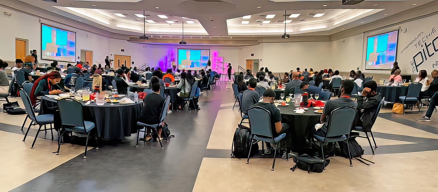 An event staged at the Anderson Center McNeil Banquet Hall that uses the East wall projection screen as the focal point for the presentation, with screens on the North and South walls providing views for attendees from any vantage point around the dining tables.