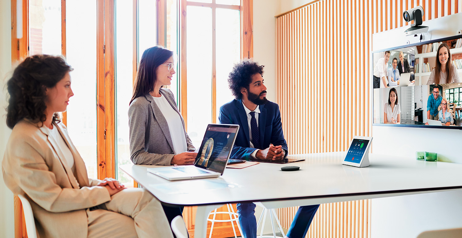 Three people in a conference room collaborating over a video call of four.